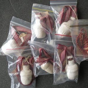 May include: Several small, white, woven bottle-shaped ornaments with red and white striped ribbon are packaged in clear plastic bags. The ornaments have a decorative, textured design.