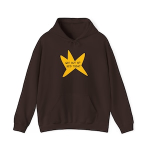 May include: A dark brown hoodie with a kangaroo pocket and a drawstring hood. The front features a yellow starburst graphic with the text "GOT OUT OF BED TODAY" in a handwritten style. The hoodie is made of a soft material.