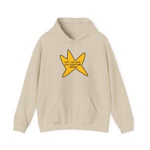 May include: A beige hoodie with a front pocket and a drawstring hood. The hoodie features a yellow star graphic with the text "LEFT THE HOUSE WITH EVERYTHING I NEEDED" in black.