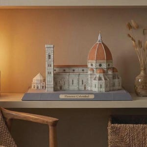 May include: A detailed paper model of the Florence Cathedral, featuring a large dome and bell tower. The model is primarily white with red and brown accents, and sits on a gray base. The text "Florence Cabredral" is visible.