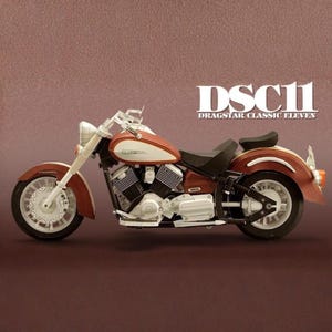 May include: A model motorcycle with a red and white fuel tank, fenders, and accents. The text "DSC11 DRAGSTAR CLASSIC ELEVEN" is displayed in white. The motorcycle has a black seat and engine components.