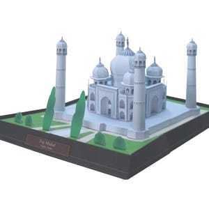 May include: A white paper model of the Taj Mahal, a famous mausoleum in Agra, India. The model is on a black base with a green lawn and trees. The base has a label that reads "Taj Mahal, Agra India."