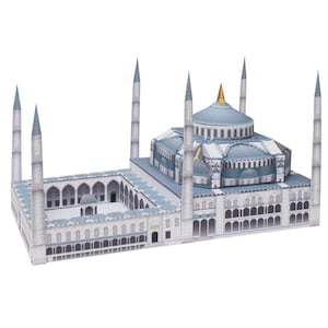 May include: A detailed paper model of a mosque, featuring light blue domes and minarets. The model includes intricate architectural details, with a courtyard and multiple arched windows. The mosque has a gold-colored dome and is set against a white background.