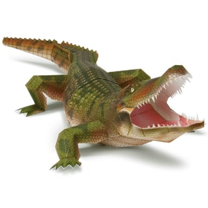 May include: A papercraft crocodile model in shades of green, brown, and orange. The crocodile has an open mouth revealing white teeth and a pink interior. The model is lying on a white surface.