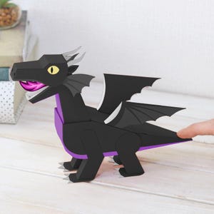 May include: A black papercraft dragon with purple accents. The dragon has a long neck, wings, and a forked tongue. The dragon's eyes are yellow. The dragon is made of folded paper and is a decorative item.
