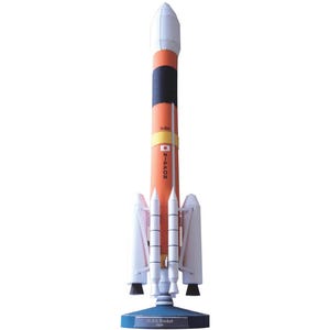May include: A model of the H-IIA Rocket from Japan, with a white nose cone, orange body with black and yellow bands, and white boosters. The rocket has the Japanese flag and the word "NIPPON" printed on its side. It sits on a blue base.