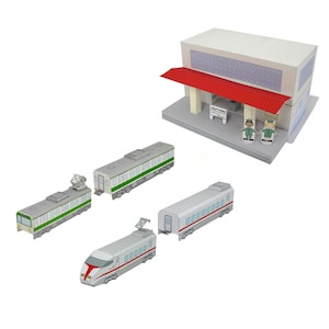 Pode incluir: Um conjunto de estação ferroviária de papel com um edifício de estação com um toldo vermelho, duas figuras de papel e quatro vagões de trem. Os vagões são brancos, verdes e cinzentos com designs detalhados.