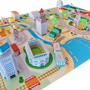 May include: A paper city playset with buildings, roads, trees, and a stadium. The set includes a helicopter, a speed limit sign, and vehicles. The buildings are in shades of white, orange, green, and purple. The set is designed for children.