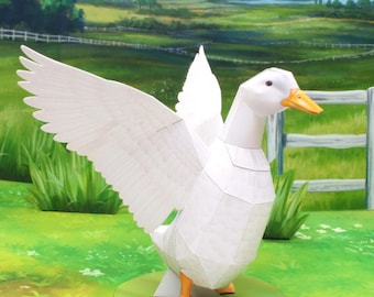 May include: A white papercraft duck with outstretched wings and orange feet. The duck is standing on a green circular base, set against a backdrop of a green field and a white fence. The duck's wings are fully extended.