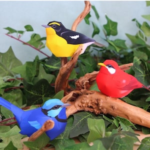 以下が含まれることがあります： 茶色の枝に止まっている、緑の葉に囲まれた3羽のカラフルな紙の鳥。鳥は黄色と黒、赤と青です。鳥は紙でできており、詳細な特徴があります。