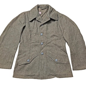 Puede incluir: Chaqueta vintage de lana verde oliva con cuello clásico, dos bolsillos delanteros y botones azul claro. La chaqueta tiene un corte entallado y mangas largas. La tela parece ser una mezcla de lana texturizada.