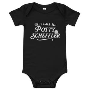Puede incluir: Body de bebé negro con el texto blanco "THEY CALL ME Potty Scheffler". Un gráfico de pelota de golf está al lado de la palabra "Potty". El body tiene mangas cortas y tres broches en la parte inferior.