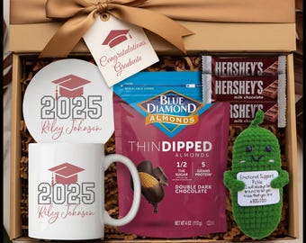 May include: A graduation gift box tied with a brown ribbon and a tag saying "Congratulations Graduate." The box contains a mug and plate with "2025 Riley Johnson", a bag of chocolate-covered almonds, Hershey's chocolate bars, and a crocheted pickle.