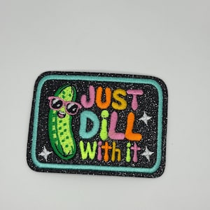 May include: A rectangular patch with a black glitter background and a teal border. The patch features a green pickle wearing pink sunglasses, with the words "JUST DILL WITH IT" in colorful letters and white star accents.