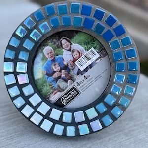 May include: Round mosaic picture frame with a family photo. The frame is decorated with blue and iridescent square tiles. The photo is 4 in x 4 in. The frame has a gray border and a Green Tree Gallery logo.