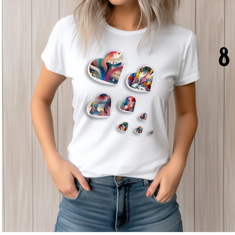 May include: White t-shirt featuring a design of colorful, abstract hearts in various sizes. The hearts have a painted appearance with a mix of vibrant colors. The shirt is paired with blue denim jeans.