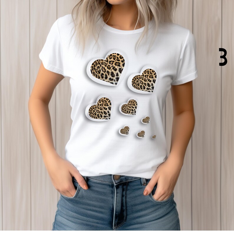 May include: White t-shirt featuring a design of leopard print hearts in various sizes. The hearts have a 3D effect with a white outline. The number "3" is printed in black on the right side of the shirt.