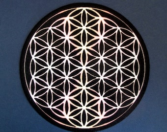 May include: A black circular mat with a white geometric pattern known as the Flower of Life. The pattern is a repeating design of overlapping circles and hexagons.