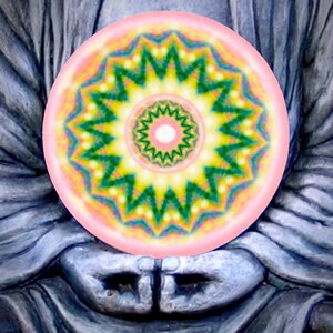 May include: A colorful, circular mandala design with a pink border and intricate patterns in green, yellow, and blue. The mandala is held in the hands of a gray statue, creating a serene and spiritual composition.