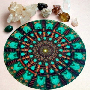 May include: A circular, patterned mat with a mandala design in shades of green, orange, and brown. Various crystals and gemstones, including quartz and malachite, are arranged around the mat, creating a spiritual or decorative theme.