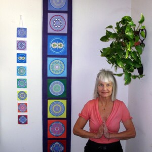 May include: A wall hanging with seven square panels, each featuring a unique mandala design in various colors. The panels are arranged vertically on a dark blue background. A smaller wall hanging with similar designs is also visible.