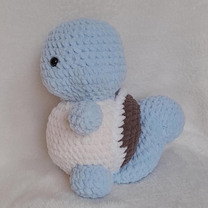 May include: A handmade, plush toy in the shape of a cartoon turtle. The turtle features a light blue head, tail, and limbs, with a white belly and a brown shell. The toy has a soft, textured appearance and a black eye.