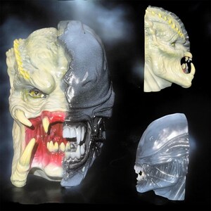 May include: A split-face mask featuring a pale, textured creature with yellow eyes and sharp fangs on the left side, and a smooth, dark gray, biomechanical creature with visible teeth on the right side, shown from front and side angles.