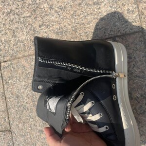 May include: A black high-top sneaker with a white rubber sole and white laces. The shoe features a side zipper closure with silver hardware. The interior zipper flap displays the text U 8800 44 and MADE IN ITALY.