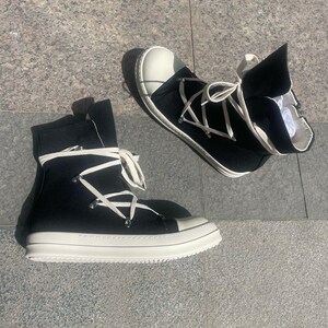 May include: A pair of black high-top canvas trainers with white laces and a white rubber sole. The laces are tied in a criss-cross pattern and the shoes have a zip on the side.