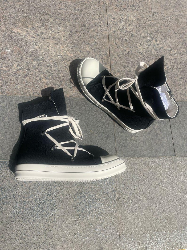 May include: A pair of black high-top canvas trainers with white laces and a white rubber sole. The laces are tied in a criss-cross pattern and the shoes have a zip on the side.