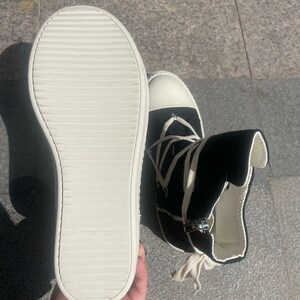 May include: A pair of black high-top canvas trainers with white laces and a white rubber sole. The trainers have a zip on the side and a white tag on the sole that says "Made in Italy".