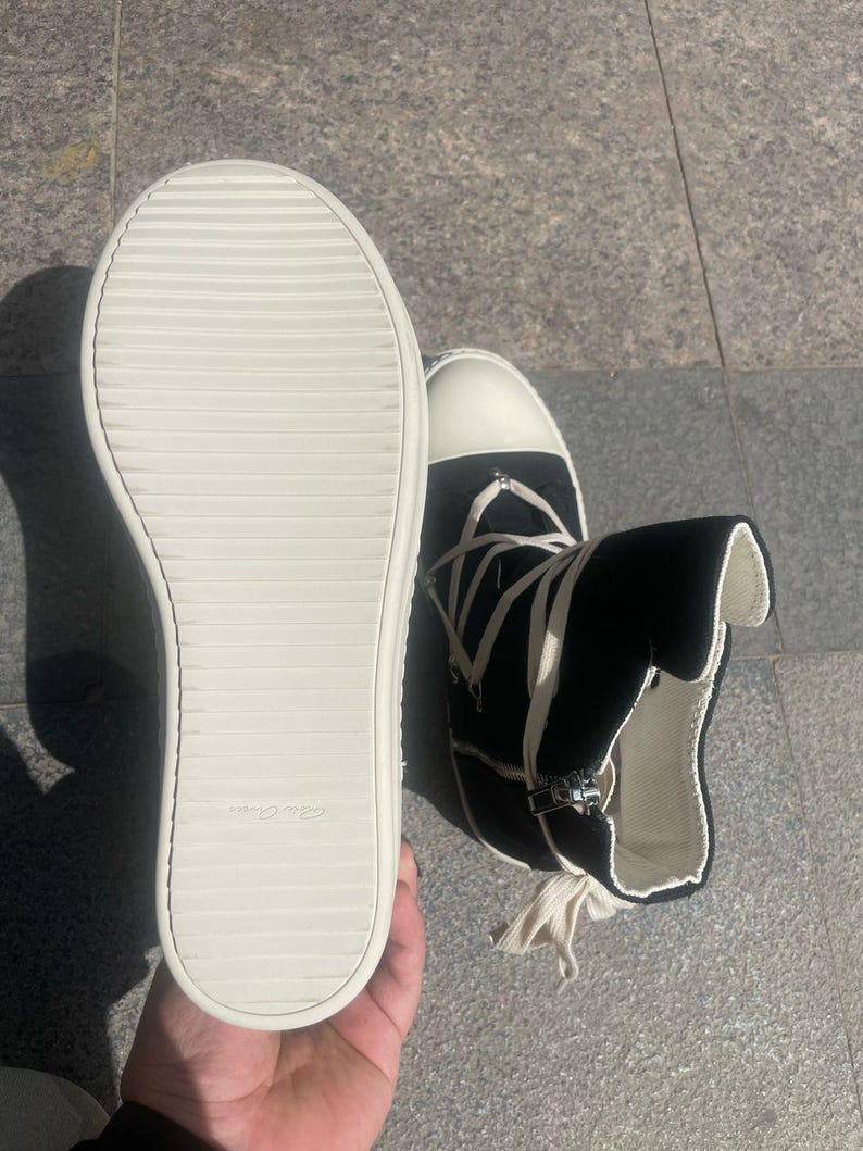 May include: A pair of black high-top canvas trainers with white laces and a white rubber sole. The trainers have a zip on the side and a white tag on the sole that says "Made in Italy".