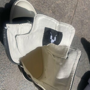May include: A pair of black and white canvas high-top trainers with a zip detail and a black logo on the inside of the shoe.