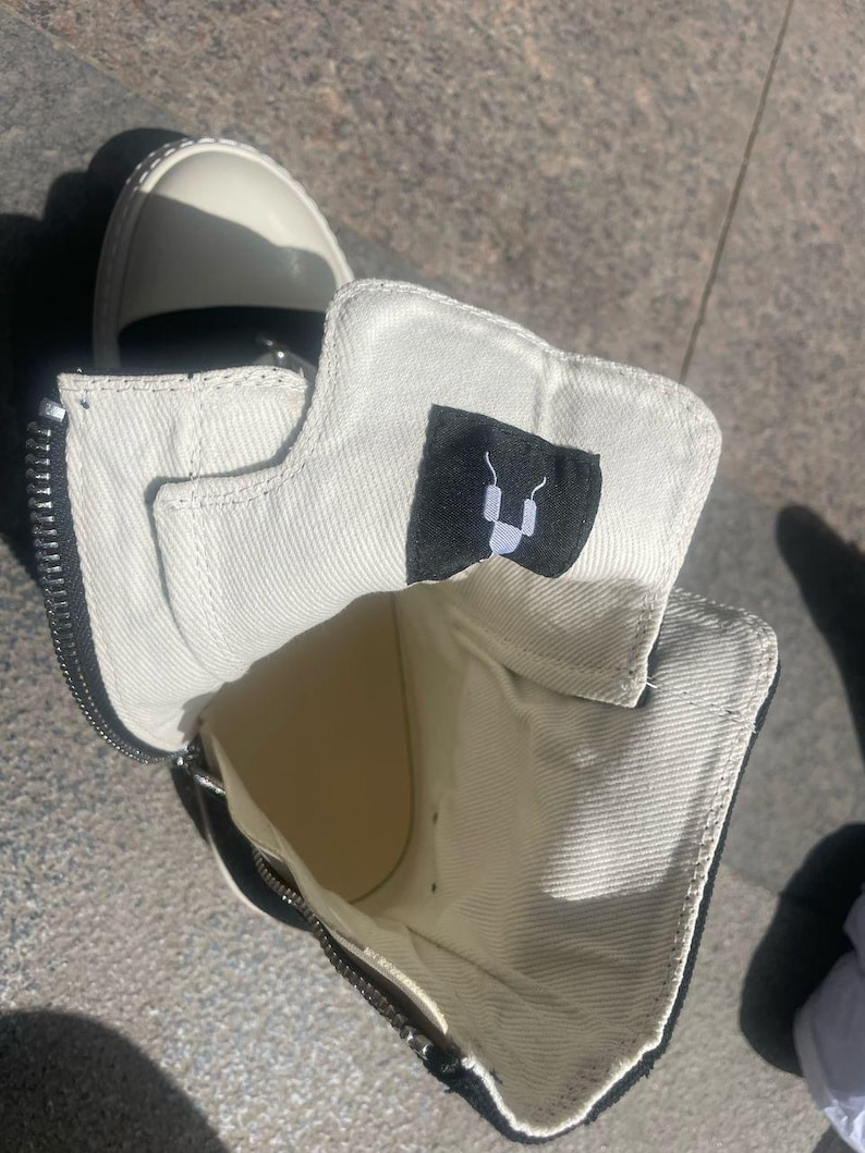 May include: A pair of black and white canvas high-top trainers with a zip detail and a black logo on the inside of the shoe.