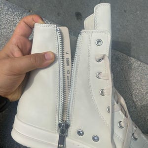 May include: Off-white high-top sneakers with a side zipper and lace-up closure. The sneakers have a thick sole and a silver zipper. The text "U 8800 43 MADE IN ITALY" is visible on the inside of the shoe.