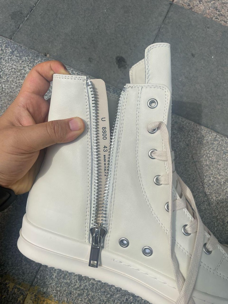 May include: Off-white high-top sneakers with a side zipper and lace-up closure. The sneakers have a thick sole and a silver zipper. The text "U 8800 43 MADE IN ITALY" is visible on the inside of the shoe.