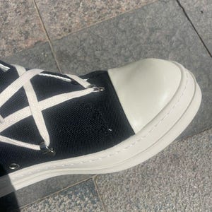 May include: Black canvas high-top trainers with white laces and a white rubber sole. The toe of the shoe is white leather.