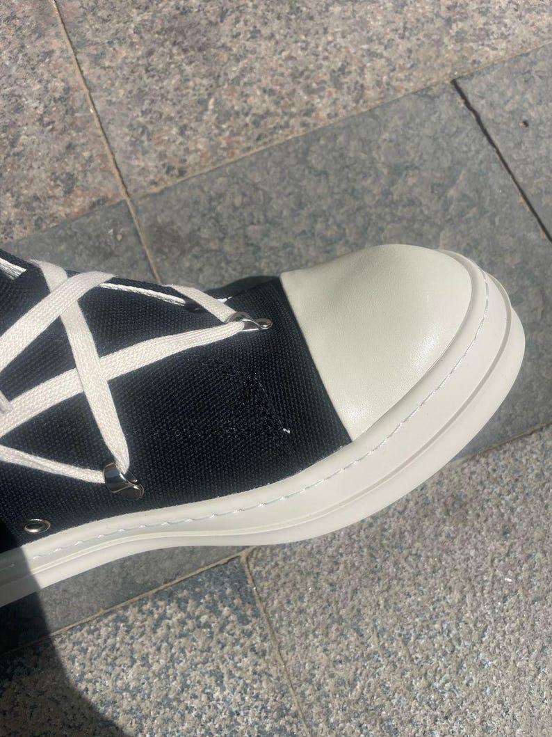 May include: Black canvas high-top trainers with white laces and a white rubber sole. The toe of the shoe is white leather.