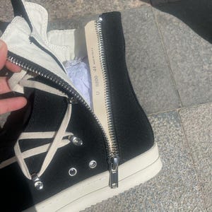 May include: Black high-top canvas sneakers with white laces and a white rubber sole. The zipper on the side of the shoe is open, revealing a label that reads "U. 88000 44 Made in Italy."