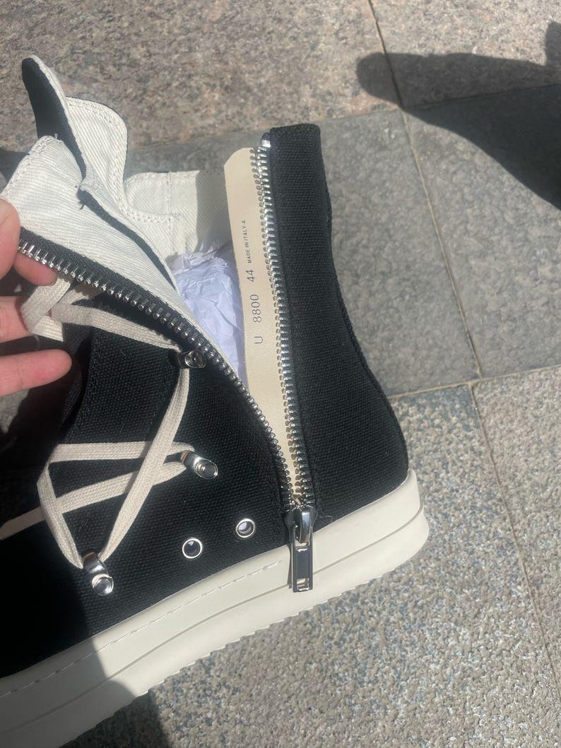 May include: Black high-top canvas sneakers with white laces and a white rubber sole. The zipper on the side of the shoe is open, revealing a label that reads "U. 88000 44 Made in Italy."