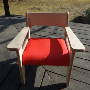 May include: A wooden chair with a red upholstered seat. The chair has a simple design with a high back and armrests.