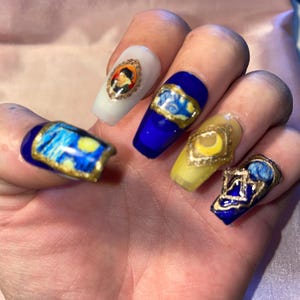 Peut inclure: Gros plan sur cinq ongles peints en bleu et jaune avec des accents dorés. Chaque ongle présente un design différent, notamment un portrait, une scène de nuit étoilée et un croissant de lune.