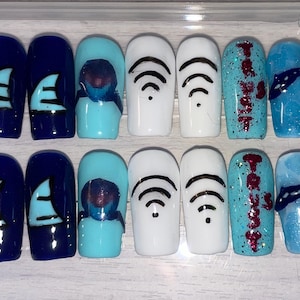 Pode incluir: Um conjunto de unhas postiças azuis, azul marinho e brancas. Os designs incluem formas geométricas pretas, uma barbatana de tubarão azul claro, o texto "Trust" em vermelho brilhante e um design azul e preto semelhante a uma bandana.