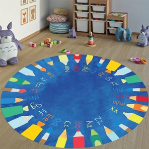 May include: A blue and yellow alphabet play mat with colorful crayons and paintbrushes around the edge. The letters of the alphabet are written in white around the edge of the mat.
