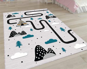 Puede incluir: Una alfombra rectangular para niños con diseño de carretera. La alfombra presenta una carretera negra que serpentea a través de un paisaje con montañas en blanco y negro, nubes verde azulado y árboles verdes. También se presenta un tipi. La alfombra es de color gris claro.