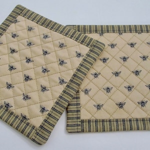 May include: Two quilted pot holders with a bee print and a green and black striped border.