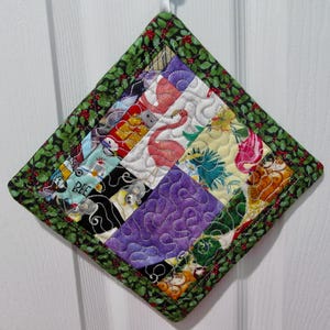Puede incluir: Un agarrador de olla acolchado con un borde de acebo verde y un diseño de patchwork con varias telas coloridas con patrones de animales y flores.