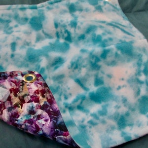 May include: A blue and white tie-dye fabric with a purple and pink floral pattern on the reverse side. The fabric has gold grommets on the edges.