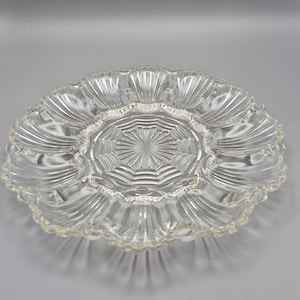 May include: Clear glass serving dish with a scalloped edge and a central starburst design. The dish has multiple compartments and a textured, ridged pattern radiating from the center. Ideal for serving appetizers or snacks.