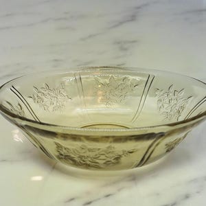 May include: A clear glass bowl with a floral pattern. The bowl is slightly yellowed and has a rounded shape.